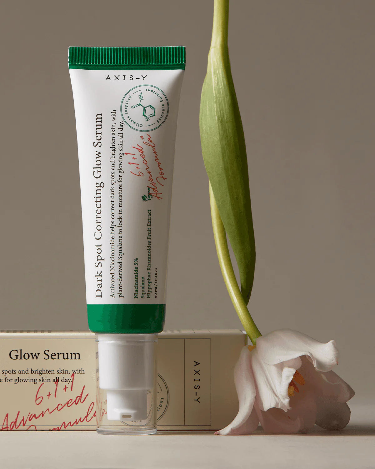 Axis-Y Dark Spot Correcting Glow Serum with a flower on a neutral background